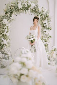 a woman standing in front of a white arch with flowers and greenery on it