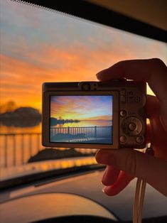 a person holding up a small camera with a sunset in the back ground behind them