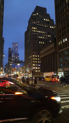 cars are driving down the street at night in front of tall buildings and skyscrapers