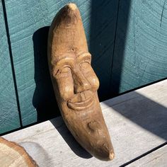 a wooden mask sitting on top of a piece of wood next to a green wall