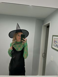 a woman wearing a witches hat taking a selfie in the mirror with her cell phone