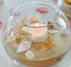 a glass bowl filled with sand and seashells on top of a white table