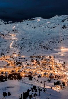 an aerial view of a town in the mountains at night with snow on the ground