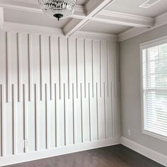 an empty room with white paneling and a chandelier