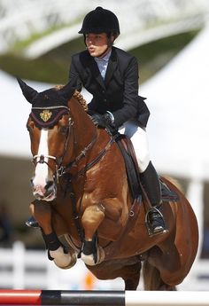 a woman riding on the back of a brown horse jumping over an obstacle with it's legs in the air