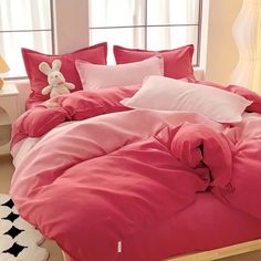 a bed with pink comforters and pillows in a room next to a white teddy bear