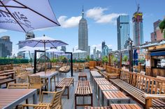 an outdoor dining area with wooden benches and umbrellas in the foreground, near skyscrapers