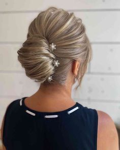 a woman with blonde hair styled into a low updo, wearing a black dress