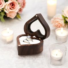 a wooden ring box sitting on top of a table next to candles