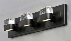 three lights on the side of a black wall mounted light fixture with clear glass shades