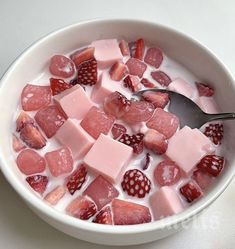 a bowl filled with fruit and ice cream on top of a white tablecloth next to a spoon