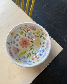 a bowl with flowers painted on it sitting on a table next to two yellow chairs