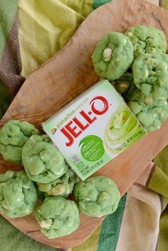 some green cookies are sitting on a wooden platter next to a carton of jello