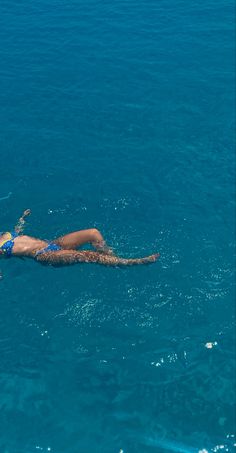 a woman is floating in the ocean on her stomach and wearing a blue swim suit