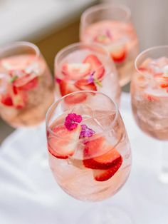 several glasses filled with ice and strawberries on top of a white cloth covered table