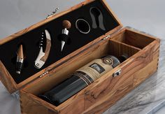 an open wooden box with wine bottles and corkscrews in it on a marble surface