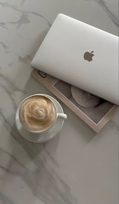 an apple laptop sitting on top of a white table next to a cup of coffee