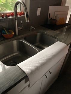 a stainless steel kitchen sink under a window next to a counter with cutting board on it