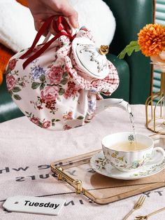 a person pouring tea into a cup and saucer on top of a table with flowers