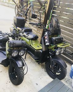 two motorcycles parked next to each other near a wooden fence with bicycles on the back