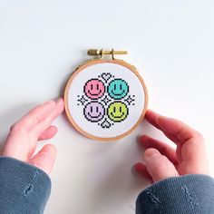 a person holding a small cross - stitched object in their left hand, with two smiley faces on it