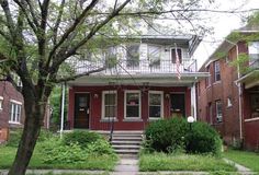 a red two story house sitting on the corner of a street in front of trees and bushes