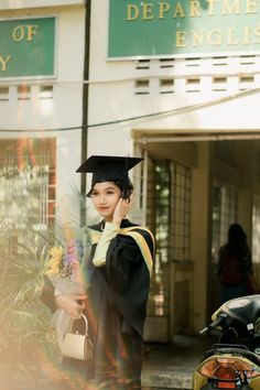 a woman in graduation cap and gown talking on her cell phone while standing next to a motorcycle