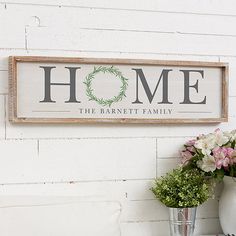 a sign that says home on the side of a white wall with flowers in vases