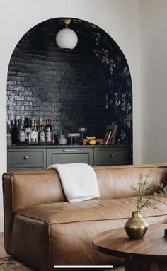 a brown leather couch sitting in front of a bar with bottles on the back wall