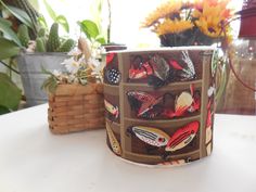 a close up of a cup on a table with flowers in the background and a basket behind it