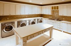 a large kitchen with white cabinets and washer and dryer in the center island