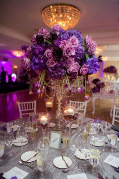 purple flowers in a tall glass vase on top of a table with place cards and wine glasses