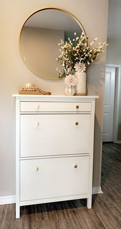 a white dresser with flowers and a round mirror