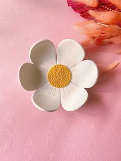 a white and yellow flower sitting on top of a pink surface next to some feathers