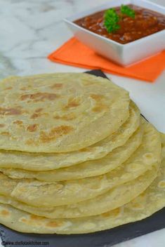 a stack of tortillas sitting on top of a cutting board next to a bowl of salsa