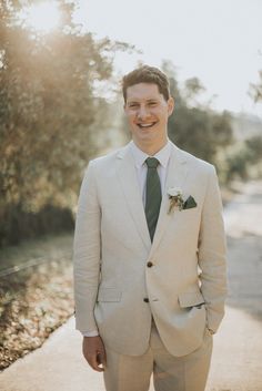 a man in a suit and tie standing on a sidewalk smiling at the camera with his hands in his pockets