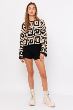 a woman in black and white sweater and shorts standing on a white background with her legs crossed