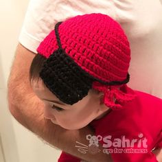 a man holding a baby wearing a crocheted red and black hat on top of his head