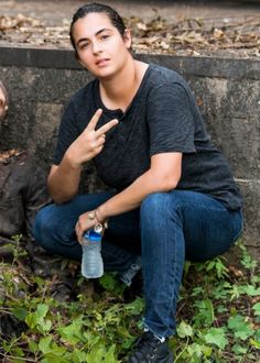 a young man sitting on the ground holding a water bottle and pointing at something in front of him