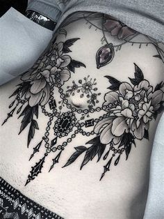 a woman's lower back tattoo with flowers and chains on her stomach, in black and white