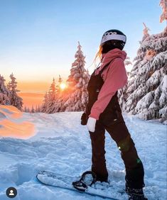 a person riding a snowboard on top of a snow covered slope with trees in the background