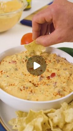 a person dipping tortilla chips into a white bowl