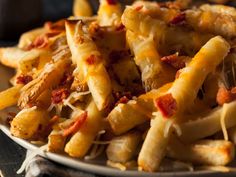 a white plate topped with cheesy pasta covered in cheese and bacon next to fries