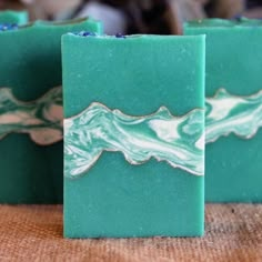 three soap bars with green and white designs on them sitting on a brown tablecloth