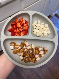 a person holding a plate with four sections filled with fruit and vegetables on top of it