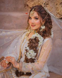 a woman with long hair wearing a white dress and veil, sitting on the ground