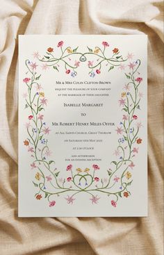 a wedding card with flowers and vines on it, sitting on top of a bed