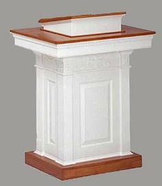 a white pedestal with a brown top and wooden trim around the base, on a gray background