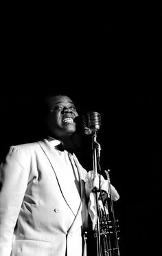 a black and white photo of a man in a tuxedo singing into a microphone