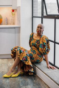 a woman sitting on a window sill in a kitchen wearing yellow shoes and a colorful dress